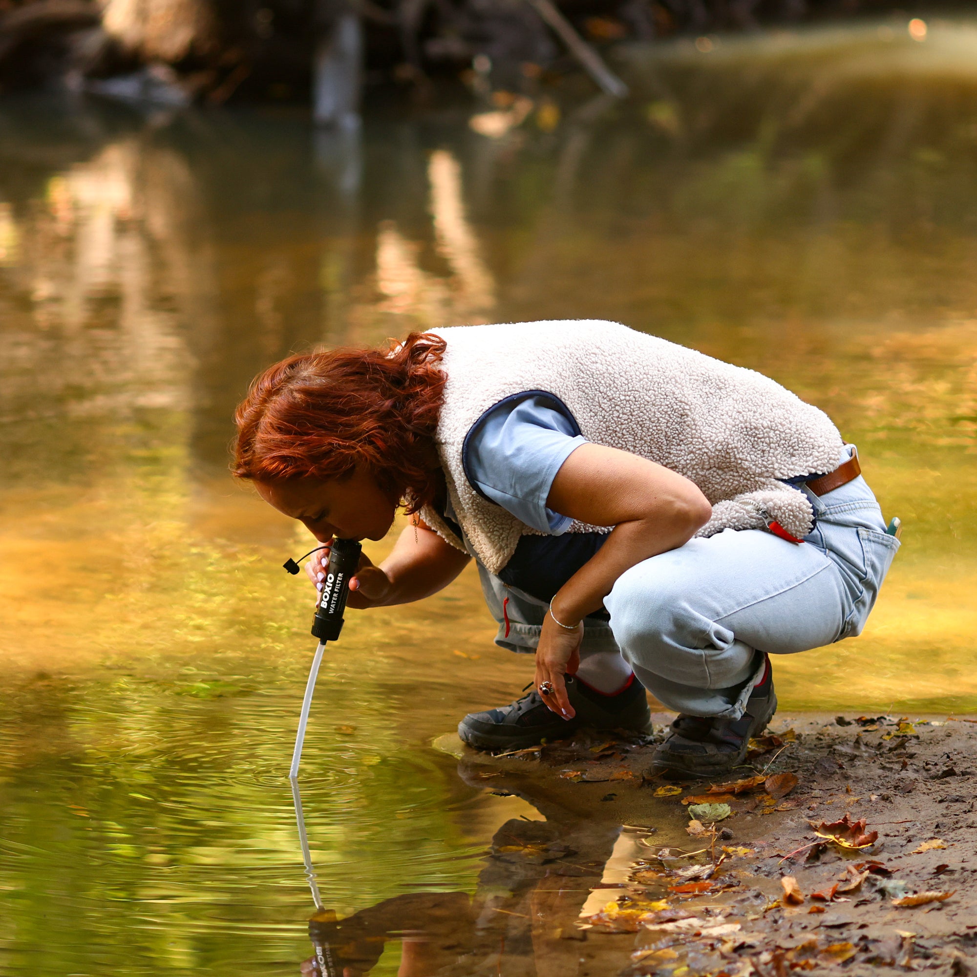 Wissenschaftlerin analysiert Wasserqualität an einem Gewässer mit einem Messgerät. Herbstliche Atmosphäre mit Laub.